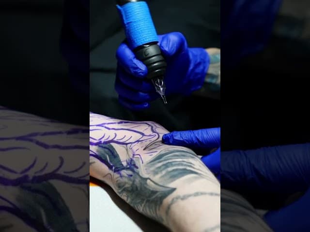 Tattoo artist working on a black and grey realism design with precise detail and care
